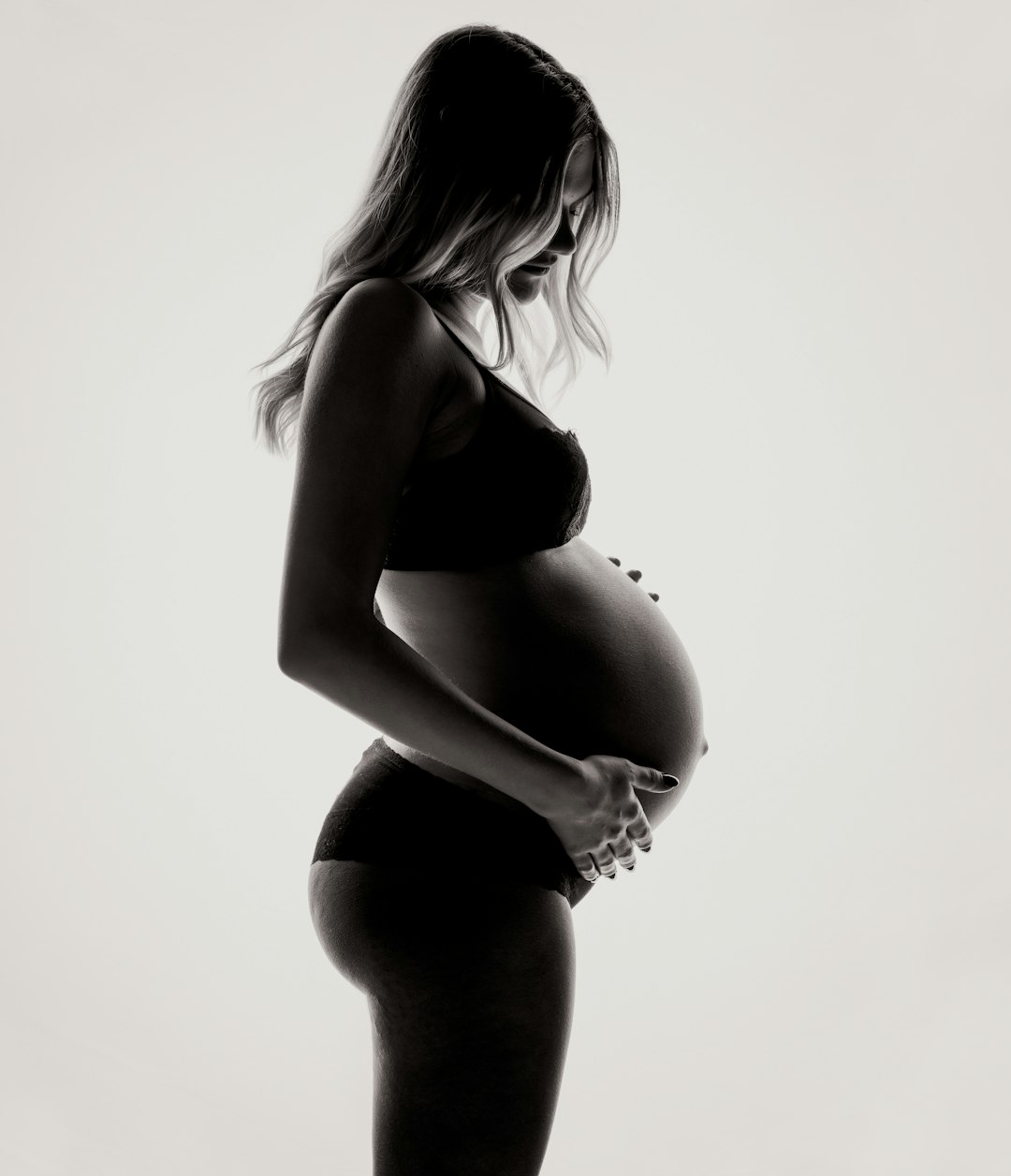 A pregnant woman in silhouette holding her belly against a bright white background