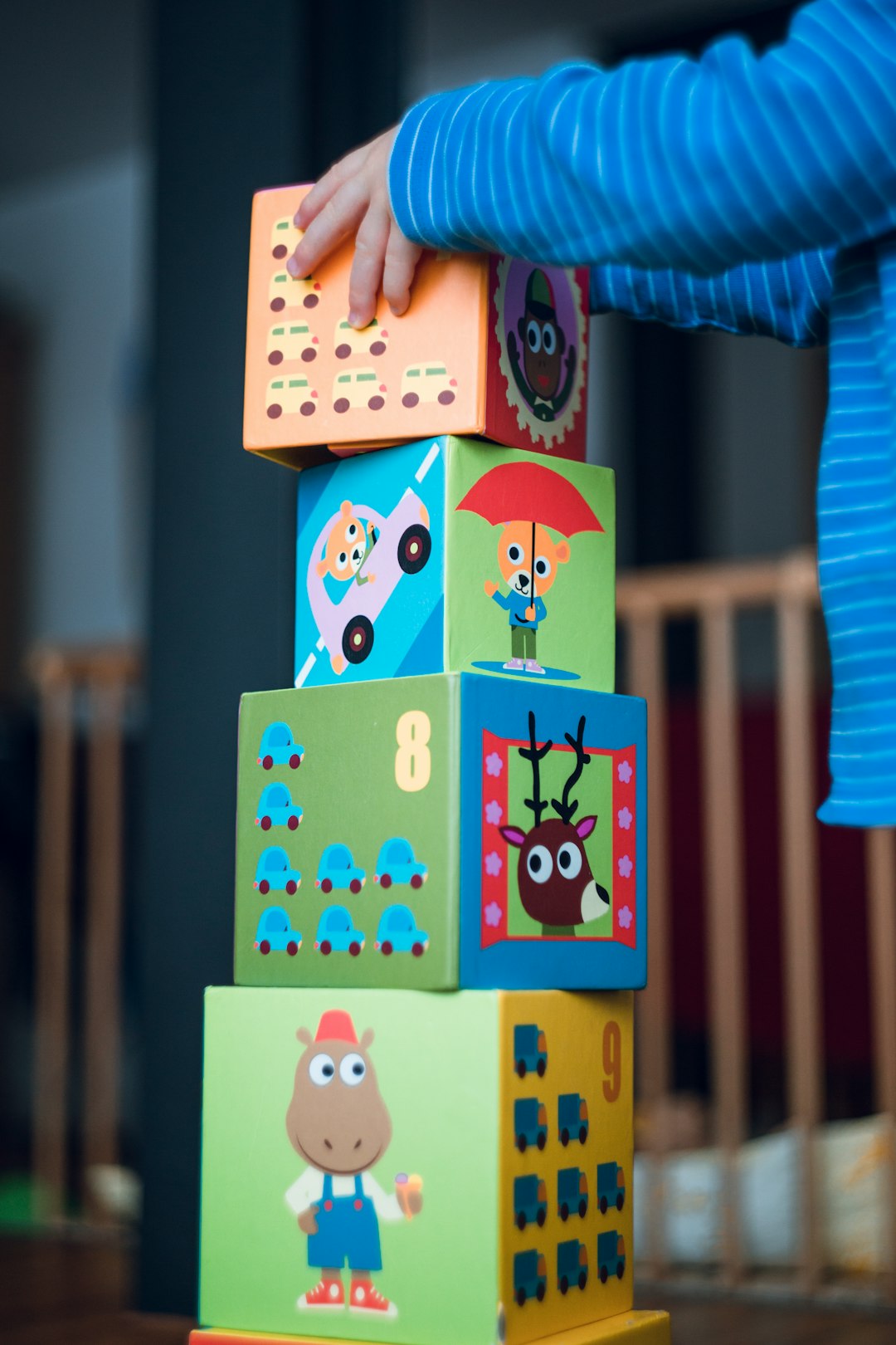 A child in a blue striped shirt stacking colorful cardboard blocks with animal illustrations